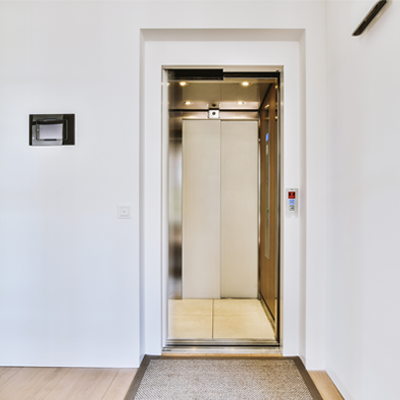 Elevator with open door in light hall with white walls and carpet in modern residential building